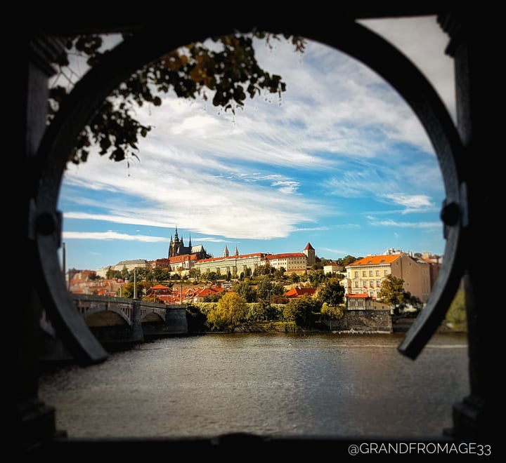 A photo taken by grandfromage33 of Prague Castle framed by a section of broken fencing. 